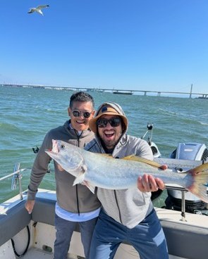 Two anglers holding a striped bass catch near the bridge